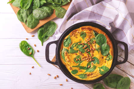 Hot homemade frittata with eggs, spinach, cheese and pine nuts in iron pan. on wooden table.Traditional Italian cuisine, healthy food concept.の写真素材