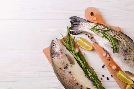 Seafood. Two raw rainbow trouts marinated with lime, peper, spices and rosemary on wooden board. Healthy food and dieting concept.の写真素材