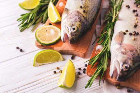 Seafood. Two raw rainbow trouts marinated with lime, peper, spices and rosemary on wooden board. Healthy food and dieting concept.の写真素材