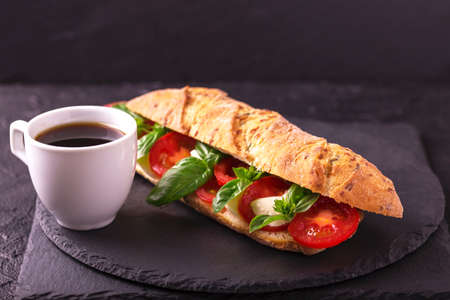 Ciabatta sandwich with caprese salad with espresso coffee on black stone table. Cherry tomatoes, green basil and mozzarella cheese. Italian food.の写真素材