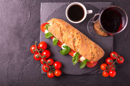 Ciabatta sandwich with caprese salad with red wine and espresso coffee on black stone table. Cherry tomatoes, green basil and mozzarella cheese. Italian food.の写真素材