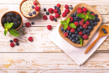 Fresh raspberry, blackberry and blueberry with mint leaves in ceramic bowls on wooden table...