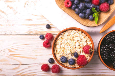 Fresh raspberry, blackberry and blueberry with mint leaves in ceramic bowls on wooden table...