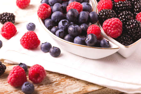 Fresh organic ripe raspberry, blackberry and blueberry in ceramic plate on wooden table background. Concept of healthy food. Top viewの写真素材