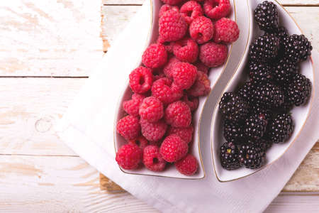 Fresh organic ripe raspberry, blackberry in ceramic plate on wooden table background. Concept of...