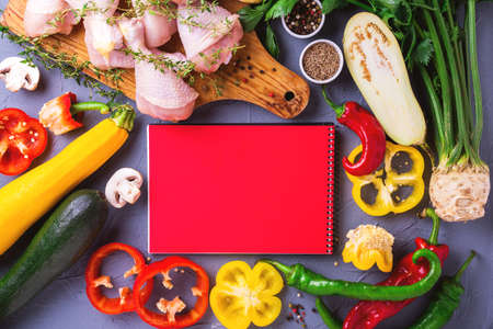 Raw chicken thighs with various vegetables ingredients around red notebook copy space for tasty diet. Top view. Food cooking ackground with copy space.の写真素材