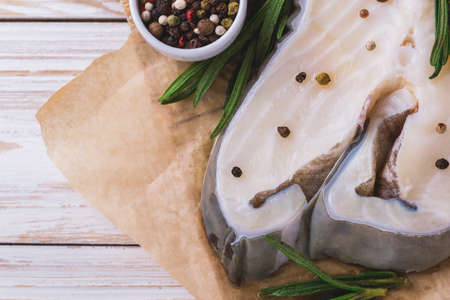 Raw fresh white fish steak with rosemary and seasoning on wooden table for tasty diet. Top view. Food cooking ackground with copy space.の写真素材