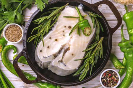 Raw fresh white fish steak with green vegetables ingredients in frying pan for tasty diet. Top view....