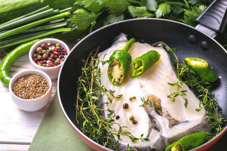 Raw fresh white fish steak with green vegetables ingredients in frying pan for tasty diet. Top view. Food cooking ackgroundの写真素材
