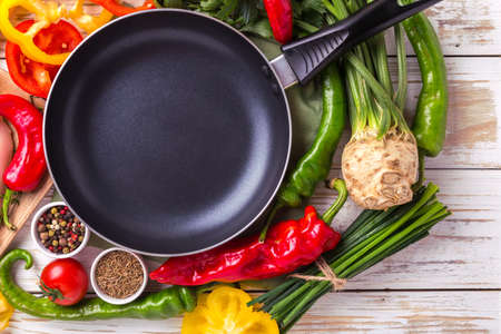 Various vegetables ingredients on wooden table around frying pan for tasty diet. Top view. Food...