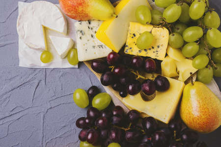 Cheese plate served with fresh grapes and pears on gray stone background. Copyspace. Top Viewの写真素材