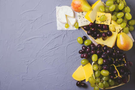 Cheese plate served with fresh grapes and pears on gray stone background. Copyspace. Top Viewの写真素材