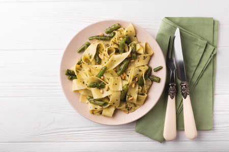 Vegetarian vegan green Italian pappardelle pasta with green bean, pesto sauce, pine nuts and ingredients. Healthy food concept. White wooden background. Top view. Copy spaceの写真素材