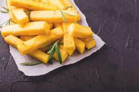 Polenta fries with sea salt, parmesan and rosemary. Italian appetizers. Fried corn sticks. Black stone background. Top view.の写真素材