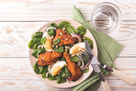 Healthy spinach salad with boiled egg, fried chiken, red onion and pine nuts. White wooden backgroundの写真素材