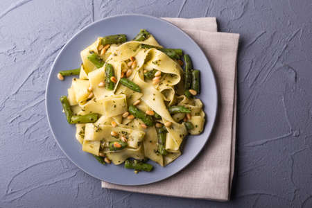 Vegetarian vegan green Italian pappardelle pasta with green bean, pesto sauce, pine nuts and ingredients. Healthy food concept. Dark background. Top view. Copy spaceの写真素材