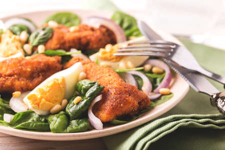 Healthy spinach salad with boiled egg, fried chiken, red onion and pine nuts. White wooden backgroundの写真素材
