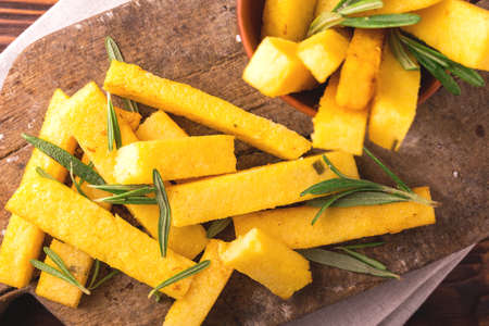 Polenta fries with sea salt, parmesan and rosemary. Italian appetizers. Fried corn sticks. Wooden background. Top view.の写真素材