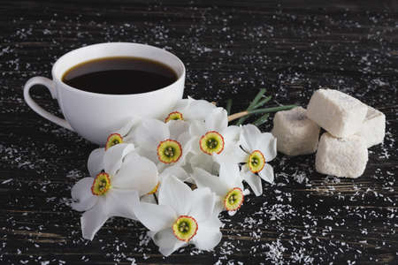 Traditional turkish dessert rahat lokum with coconut, and narcissus and cup of coffee on black wooden backgroundの写真素材