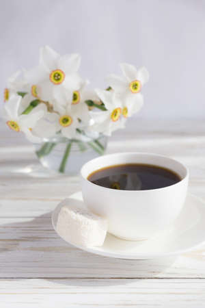 Traditional turkish dessert rahat lokum with coconut, and narcissus and cup of coffee on white wooden backgroundの写真素材