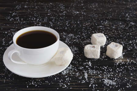 Traditional turkish dessert rahat lokum with coconut and cup of coffee on black wooden background