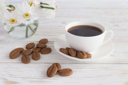 cookies and narcissus and cup of coffee on white wooden background