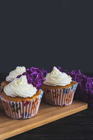 Homemade tiramisu cupcakes with whipped cream and bouquet of purple lilac spring flowers on rustic wooden backgroundの写真素材