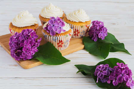 Homemade tiramisu cupcakes with whipped cream and bouquet of purple lilac spring flowers on rustic wooden backgroundの写真素材