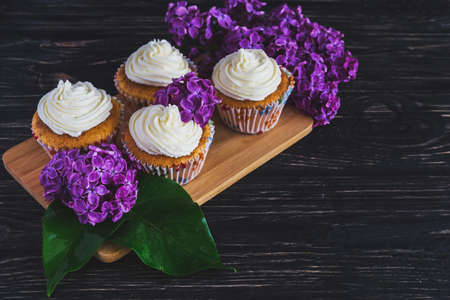 Homemade tiramisu cupcakes with whipped cream and bouquet of purple lilac spring flowers on rustic wooden backgroundの写真素材