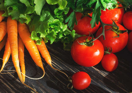 Concept of vegetarian food with  tomatoes on vine, carrots and green salad on black rustic wooden backgroundの写真素材
