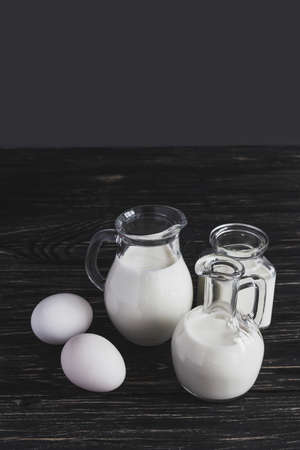 Three glass jars with milk and eggs on white wooden backgroundの写真素材