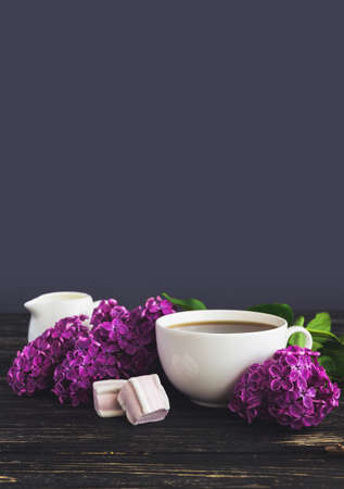 Cup of coffee, marshmallow and bouquet of purple lilac spring flowers on rustic wooden backgroundの写真素材