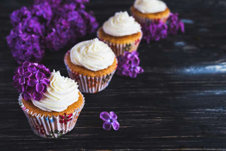 Homemade tiramisu cupcakes with whipped cream and bouquet of purple lilac spring flowers on rustic wooden backgroundの写真素材