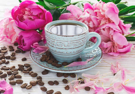 Cup of coffee, coffee beans and bouquet of peonies on rustic wooden backgroundの写真素材