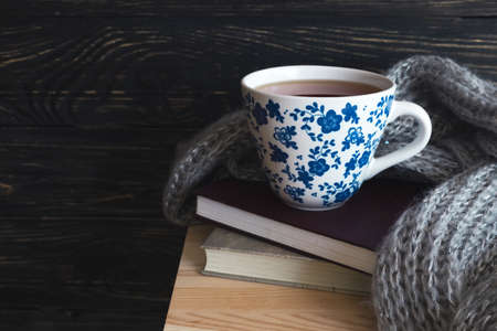 Warm knitted plaid, cup of hot tea and books on wooden table. Background with copy Space.の写真素材