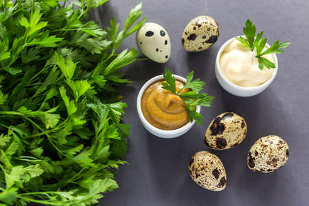 Fresh homemade sauces yellow mustard and white mayonnaise. Spices, quail eggs and parsley on dark...