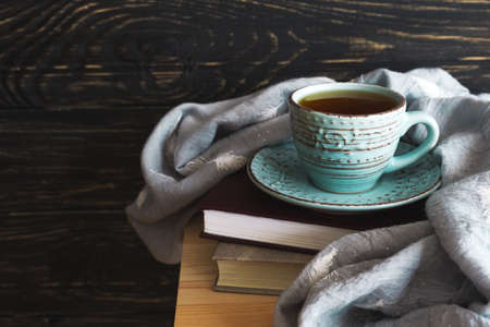 Warm knitted plaid, cup of hot tea and books on wooden table. Background with copy Space.の写真素材