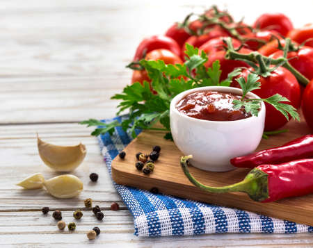 Ketchup. Tomato sauce salsa, hot chili, parsley, fresh tomatoes on vine, garlic, and spices, allspice, on wooden background.の写真素材