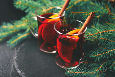 Hot mulled wine with orange, anise, cardamon and cinnamon on slate marble background. Christmas tree branches and cones. Flat lay, copy space, horizontal view. Holidays.の写真素材