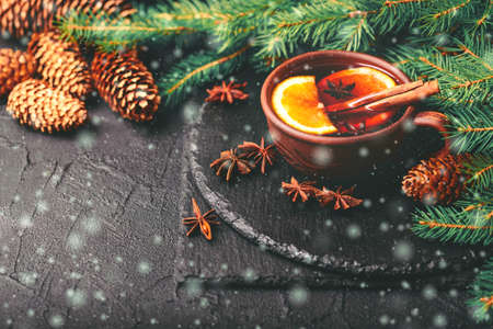 Hot mulled wine with orange, anise, cardamon and cinnamon on slate marble background. Christmas tree branches and cones. Flat lay, copy space, horizontal view. Holidays.の写真素材