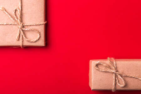 Gift box wrapped in recycled paper with ribbon bow on red background. Flat lay, copy space, top view. Color surge trend.の写真素材