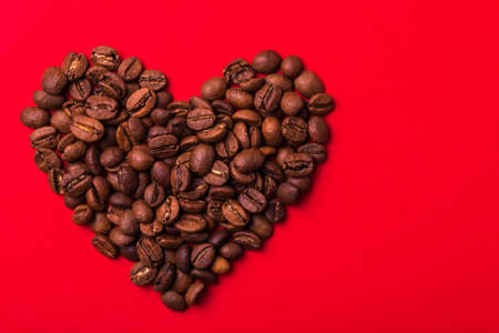 Roasted coffee beans in heart shape isolated on red background. Color surge trend. Valentine's day concept. Macroの写真素材
