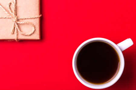 Gift box wrapped in recycled paper with ribbon bow  and cup of espresso coffee on red background. Flat lay, copy space, top view. Color surge trend.の写真素材