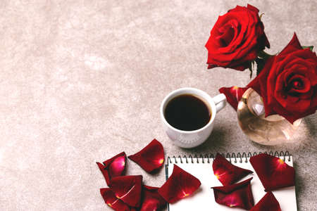 Empty notebook, pen, red roses and coffee on gray stone background. Workplace. Top viewの写真素材