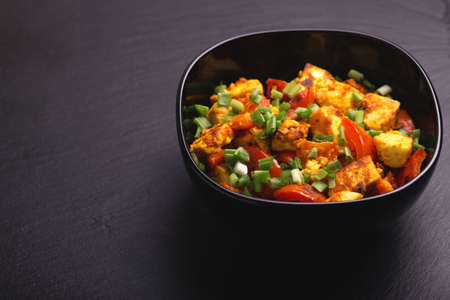 Indian cuisine. Paneer Tikka Kabab with chilli pepper, onions and curry sauce on black background. Asian salad. Top view. Copy spaceの写真素材