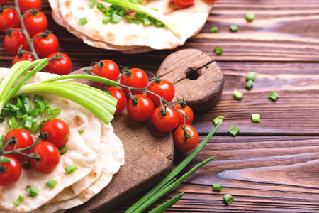 Traditional Kerala Indian cuisine. Homemade flatbread chapati with green onion and cherry tomato on dark wooden background. Copyspace, top view, flatlay.の写真素材