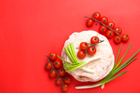 Traditional Kerala Indian cuisine. Homemade flatbread chapati with green onion and cherry tomato on red background. Copyspace, top view, flatlay. Color surge trend.の写真素材