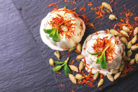 Traditional Rajasthani Indian cuisine. Homemade kulfi dessert, ice cream with safron, mint and nuts on black slate background. Copyspace, top view.の写真素材