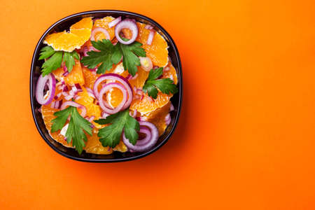 Traditional Italian Sicilian cuisine. Healthy orange salad with red onion, parsley and vinegar in black bowl on orange background. Copyspace, top view.の写真素材