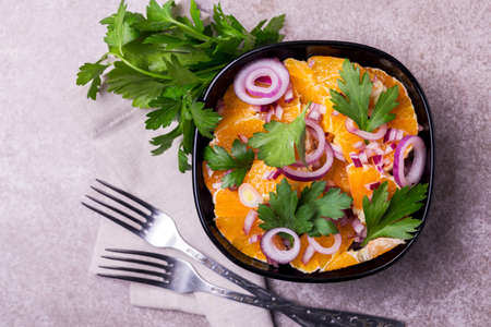 Traditional Italian Sicilian cuisine. Healthy orange salad with red onion, parsley and vinegar in black bowl on gray slate background. Copyspace, top view.の写真素材